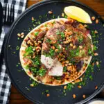 Overhead sumac chicken musakhan with caramelised onions, pine nuts and yoghurt served on flatbread.