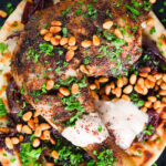 Close-up overhead sumac chicken musakhan with caramelised onions, pine nuts and yoghurt served on flatbread.