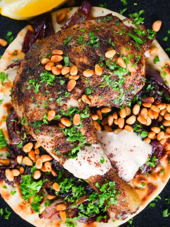 Close-up overhead sumac chicken musakhan with caramelised onions, pine nuts and yoghurt served on flatbread.