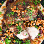 Close-up overhead sumac chicken musakhan with caramelised onions, pine nuts and yoghurt served on flatbread.
