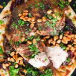 Close-up overhead sumac chicken musakhan with caramelised onions, pine nuts and yoghurt served on flatbread.