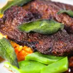 Close-up calves liver, an onion and bacon gravy, swede and carrot mash, beans and sage.