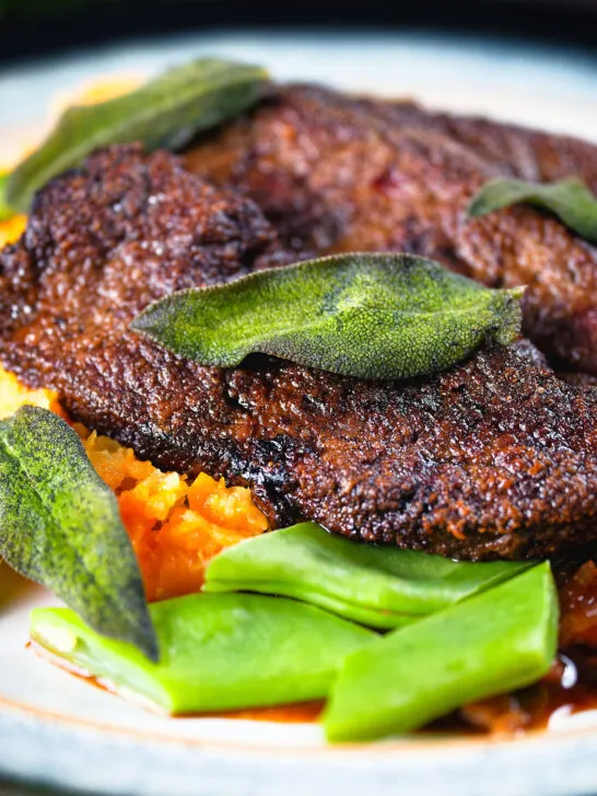Close-up calves liver, an onion and bacon gravy, swede and carrot mash, beans and sage.