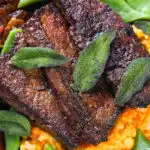 Overhead close-up calves liver, an onion and bacon gravy, swede and carrot mash, beans and sage.