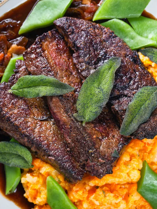 Overhead close-up calves liver, an onion and bacon gravy, swede and carrot mash, beans and sage.
