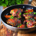 Roasted honey and harissa chicken thighs with red onions cooked in a small frying pan.