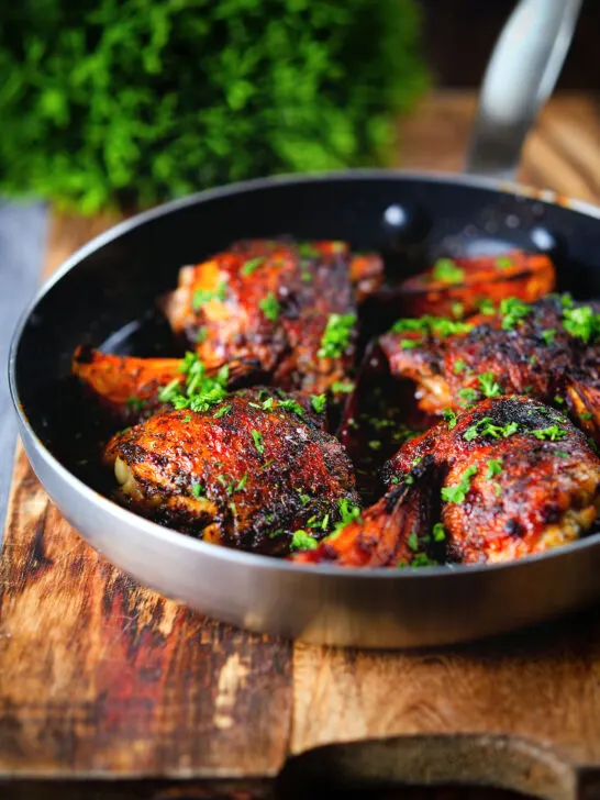 Roasted honey and harissa chicken thighs with red onions cooked in a small frying pan.