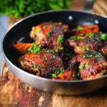 Roasted honey and harissa chicken thighs with red onions cooked in a small frying pan.