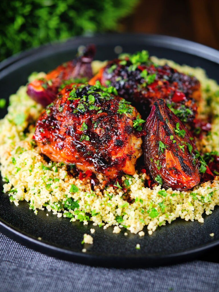 Roasted honey and harissa chicken thighs with red onions and herby couscous.