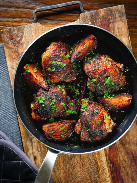 Overhead roasted honey and harissa chicken thighs with red onions cooked in a small frying pan.