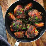 Overhead roasted honey and harissa chicken thighs with red onions cooked in a small frying pan.
