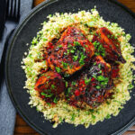 Overhead roasted honey and harissa chicken thighs with red onions and herby couscous.