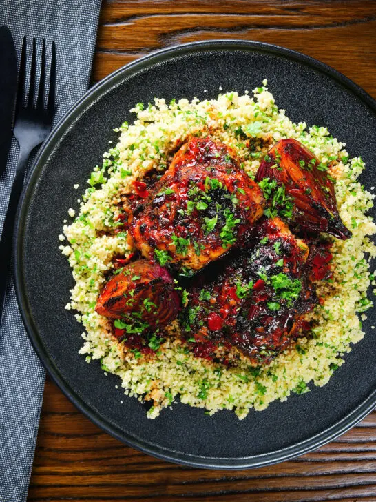 Overhead roasted honey and harissa chicken thighs with red onions and herby couscous.