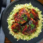Overhead roasted honey and harissa chicken thighs with red onions and herby couscous.