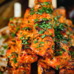 Close-up Indian salmon tikka skewers served with roti and mint raita.