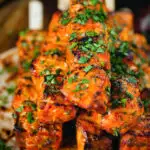 Close-up Indian salmon tikka skewers served with roti and mint raita.