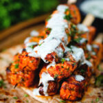Indian salmon tikka kebab skewers served with roti and drizzled with mint raita.