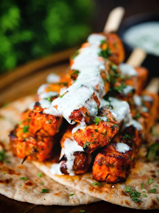 Indian salmon tikka kebab skewers served with roti and drizzled with mint raita.