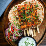 Overhead Indian salmon tikka skewers served with roti, kachumber salad and mint raita.