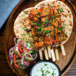 Overhead Indian salmon tikka skewers served with roti, kachumber salad and mint raita.