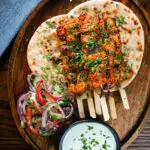 Overhead Indian salmon tikka skewers served with roti, kachumber salad and mint raita.