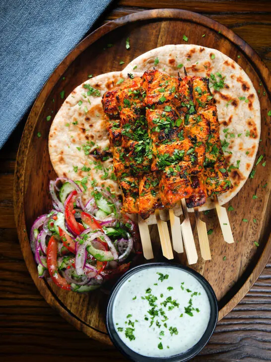 Overhead Indian salmon tikka skewers served with roti, kachumber salad and mint raita.