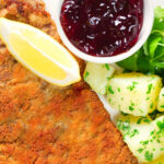 Overhead close-up breaded veal Wiener schnitzel served with parsley buttered potatoes and redcurrant jelly.