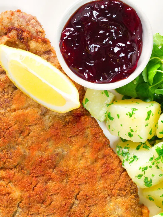 Overhead close-up breaded veal Wiener schnitzel served with parsley buttered potatoes and redcurrant jelly.