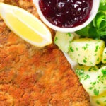 Overhead close-up breaded veal Wiener schnitzel served with parsley buttered potatoes and redcurrant jelly.