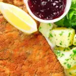 Overhead close-up breaded veal Wiener schnitzel served with parsley buttered potatoes and redcurrant jelly.