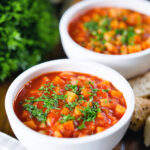 Vegetarian winter root vegetable soup served with bread and fresh parsley.