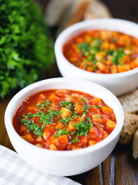 Vegetarian winter root vegetable soup served with bread and fresh parsley.