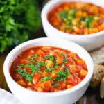 Vegetarian winter root vegetable soup served with bread and fresh parsley.