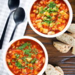 Overhead vegetarian winter root vegetable soup served with bread and fresh parsley.
