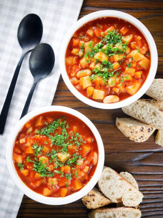 Overhead vegetarian winter root vegetable soup served with bread and fresh parsley.