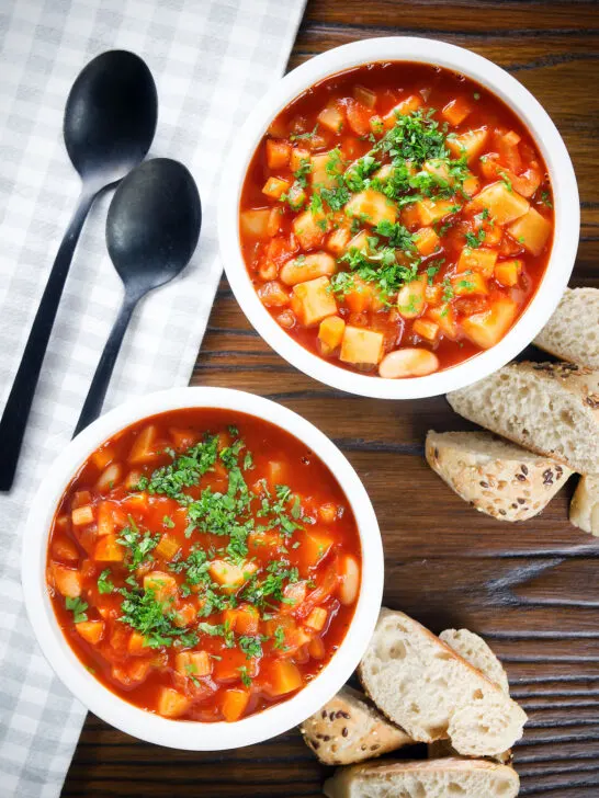 Overhead vegetarian winter root vegetable soup served with bread and fresh parsley.