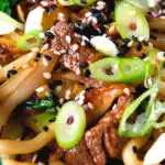 Close-up beef yaki udon, stir fry noodles garnished with spring onions and sesame seeds.