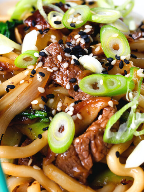 Close-up beef yaki udon, stir fry noodles garnished with spring onions and sesame seeds.