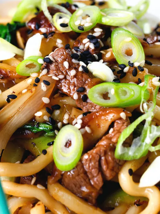 Close-up beef yaki udon, stir fry noodles garnished with spring onions and sesame seeds.