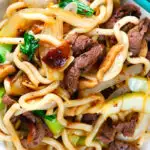 Close-up overhead beef yaki udon noodles garnished with spring onions and sesame seeds.