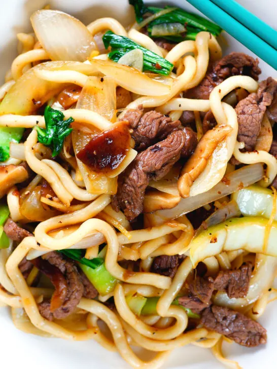 Close-up overhead beef yaki udon noodles garnished with spring onions and sesame seeds.