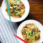Overhead beef yaki udon noodles garnished with spring onions and sesame seeds.
