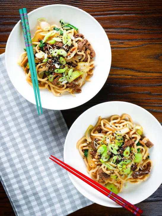 Overhead beef yaki udon noodles garnished with spring onions and sesame seeds.
