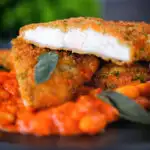 Breaded and fried chicken Milanese cut open to show the texture, served with fagioli all'uccalletto.