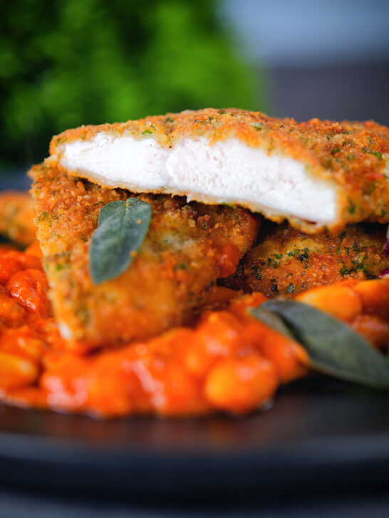 Breaded and fried chicken Milanese cut open to show the texture, served with fagioli all'uccalletto.