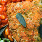 Overhead close-up breaded and fried chicken Milanese served with Italian inspired fagioli all'uccalletto.