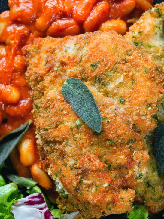 Overhead close-up breaded and fried chicken Milanese served with Italian inspired fagioli all'uccalletto.