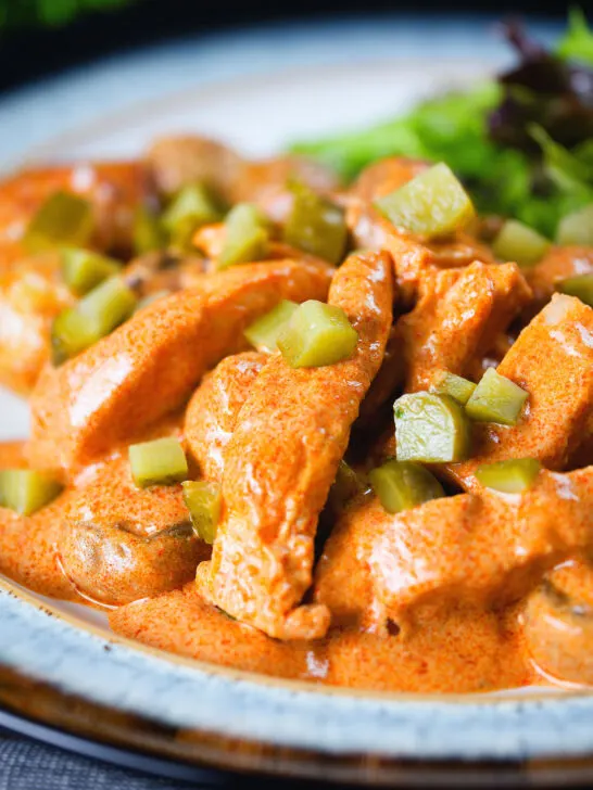 Close-up chicken and mushroom stroganoff served with chopped gherkins.