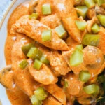 Overhead close-up chicken and mushroom stroganoff served with fried potatoes and chopped gherkins.