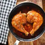 Overhead poulet au vinaigre, chicken legs in garlic, shallots and vinegar in a pan.